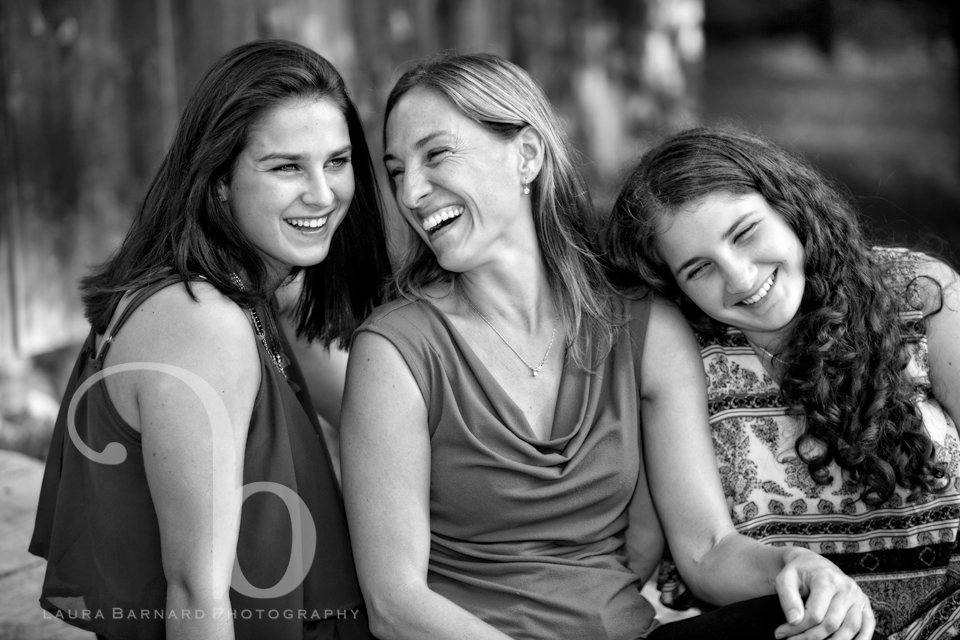 A mother and her two daughters laughing together outdoors, black and white.