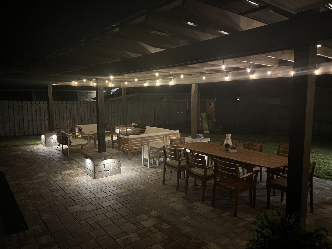 A covered patio at night, lit by string lights and low lights set into stone pillars