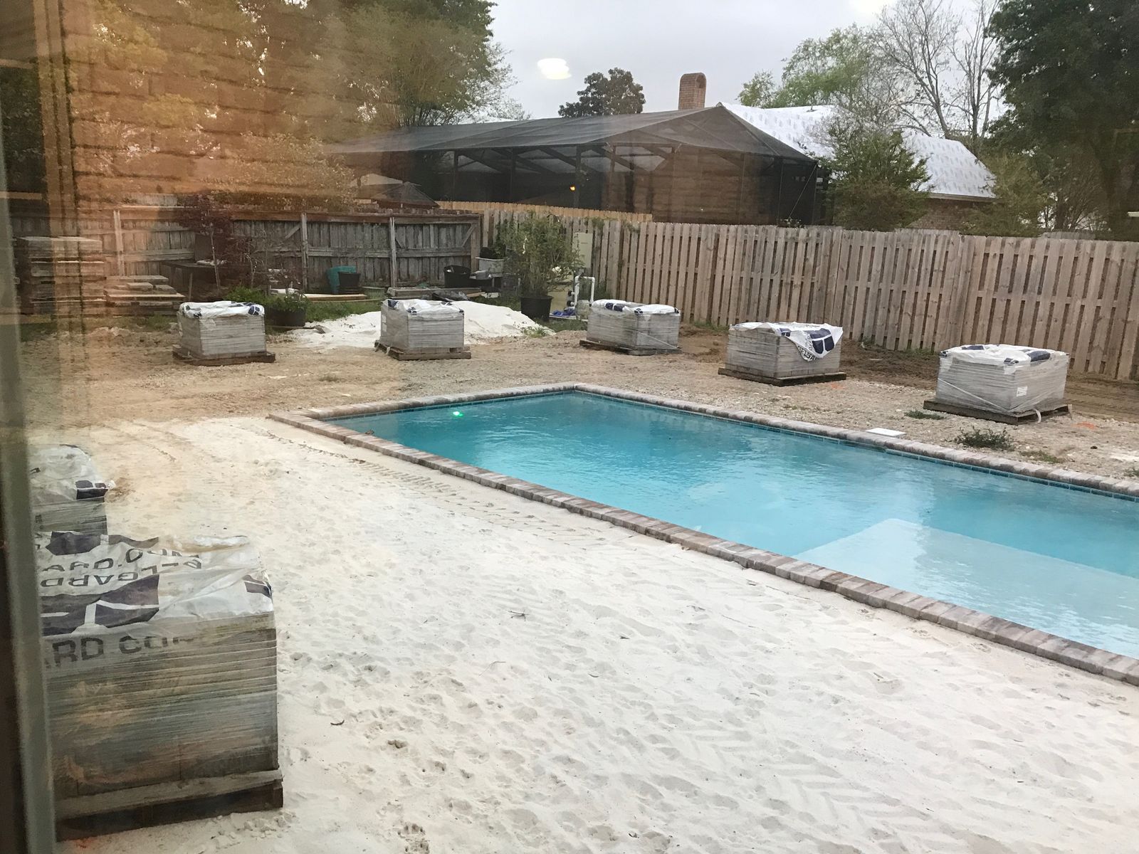 Before: a new pool surrounded by bare sand, with pallets of pavers waiting along the fence